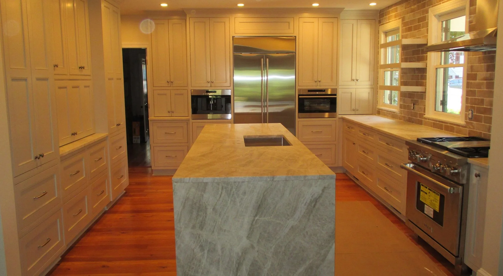 A long custom kitchen with a stone waterfall island and full height cabinetry