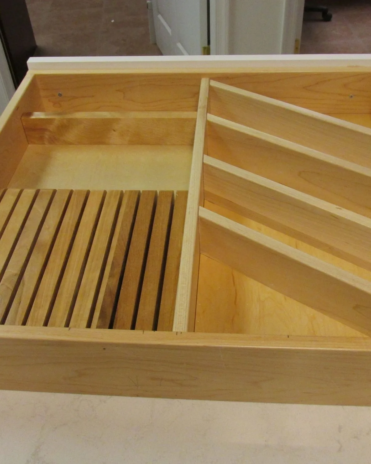 A maple drawer divided into fitted compartments with a slatted rack