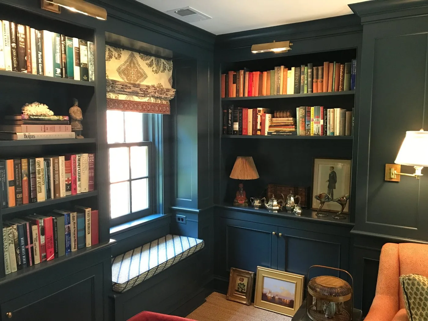 A library with dark painted floor to ceiling shelving and a window seat